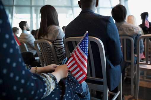 Person holding an American flag in a metal chair at a meeting. 