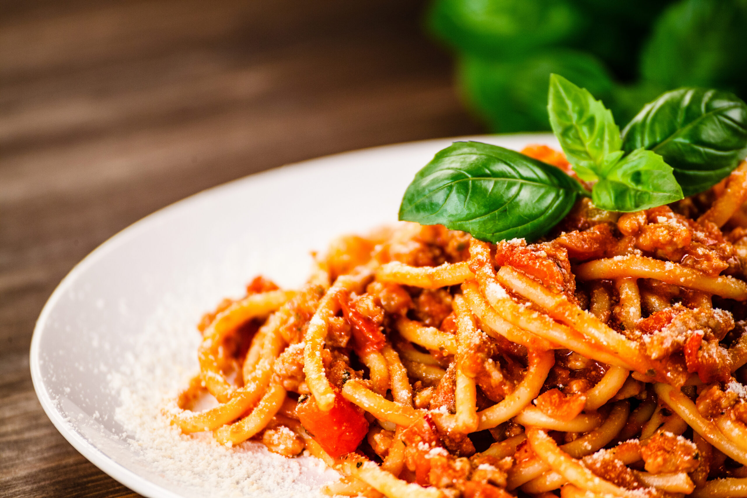 Pasta Bolognese on a white plate and a green basil leaf.