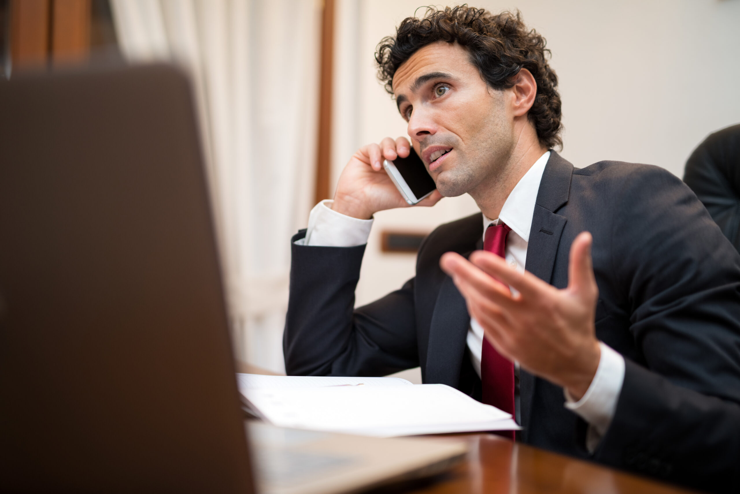 Man in a suit and a red tie talking on the phone.